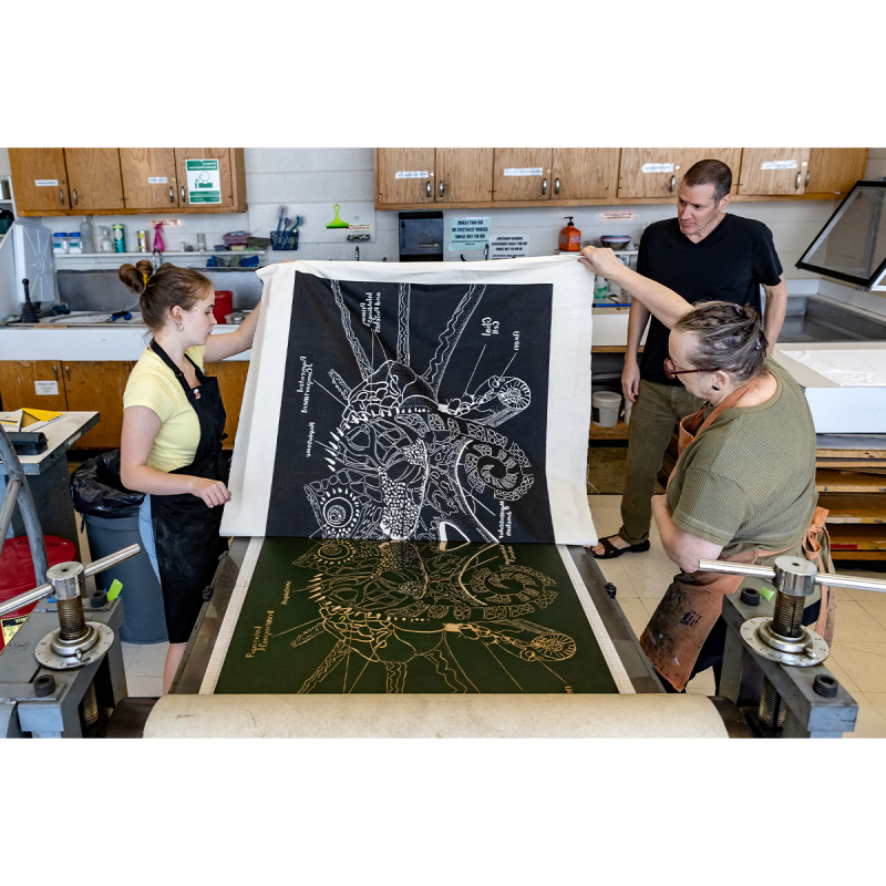 Bob Goldstein and Beth Grabowski helping a student hold off a large piece of art.